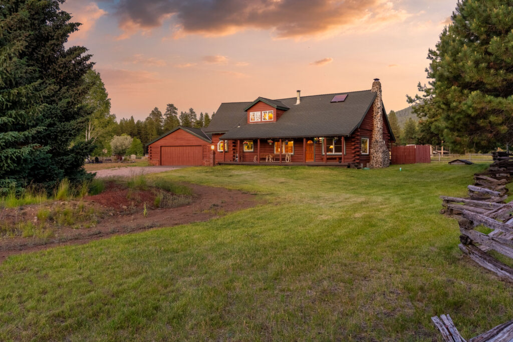 Log home at sunset across an open meadow ringed by pines