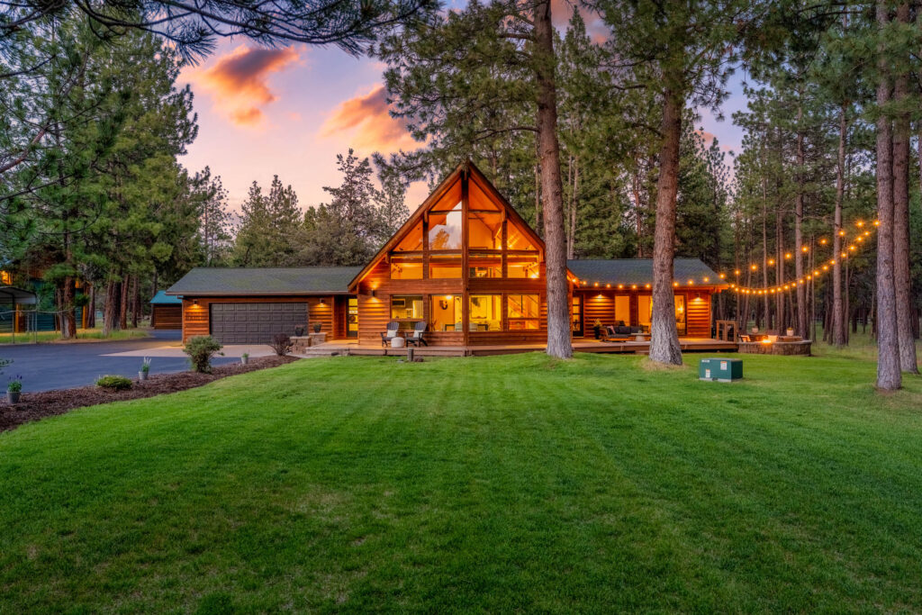 Twilight front exterior of a timber lodge home with lit windows and manicured lawn