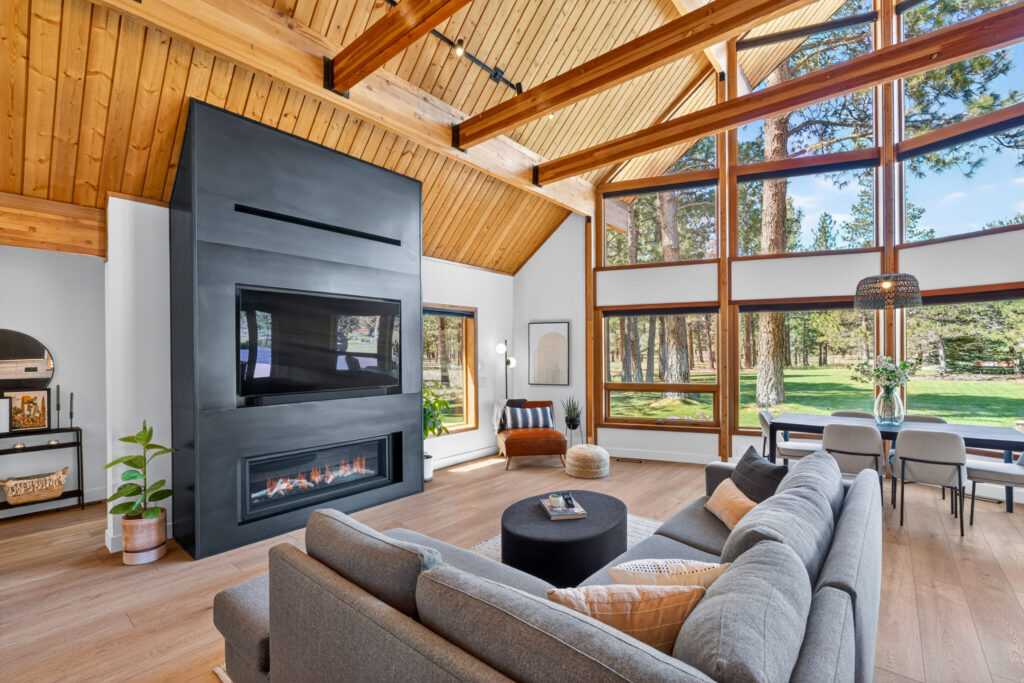 Bright living room with fireplace and floor-to-ceiling windows opening to the forest