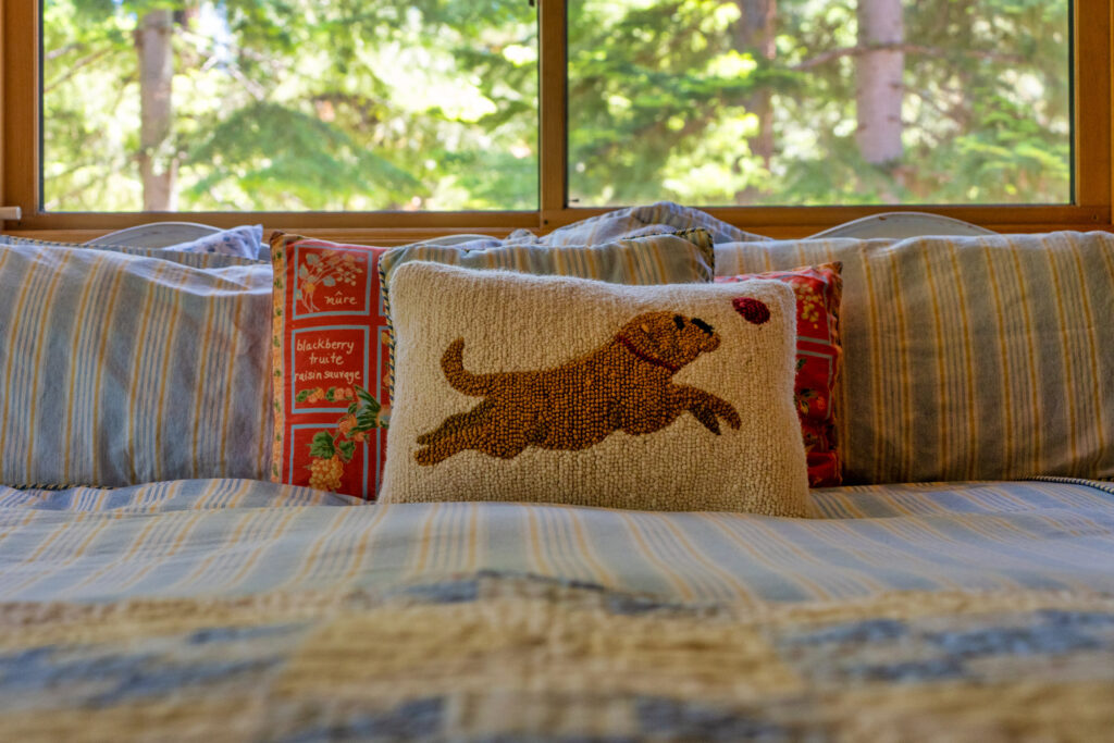 Cozy bedroom with striped bedding and a dog pillow framed by forest windows