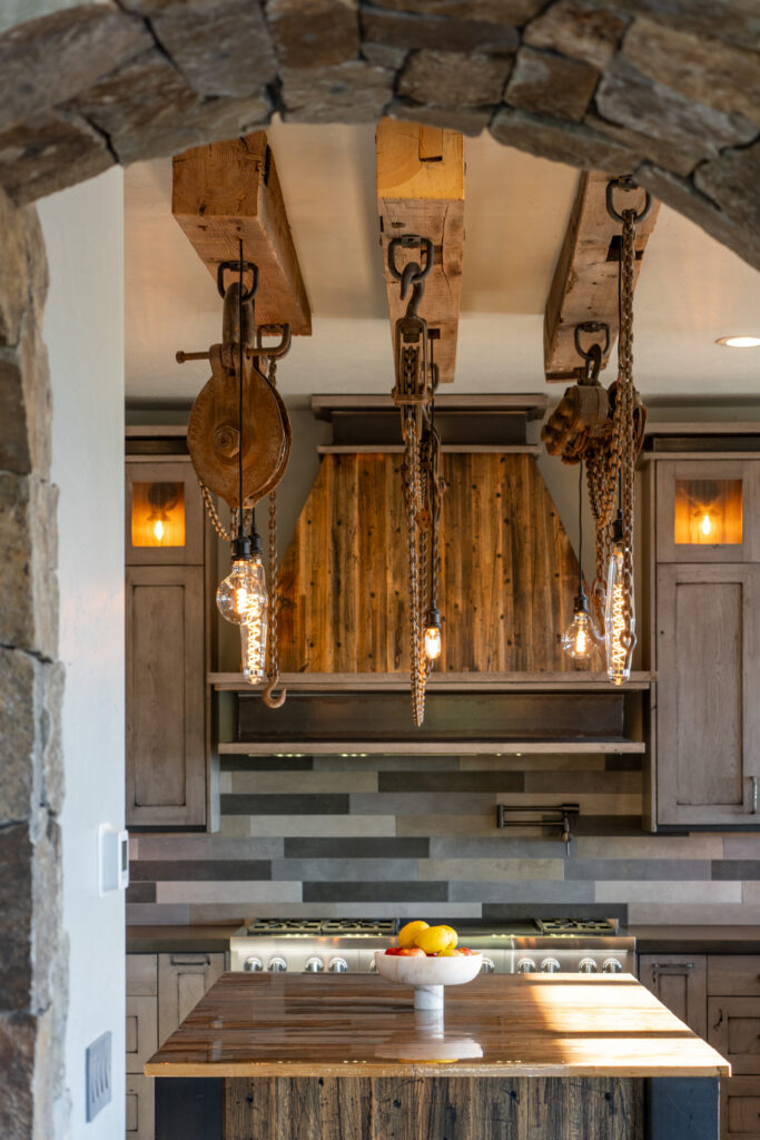 Rustic kitchen with reclaimed-beam range hood, pulley pendant lights and stone archway