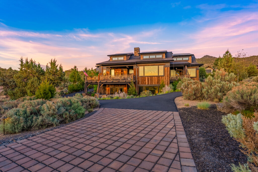 Hilltop home glowing at twilight above a long paver driveway