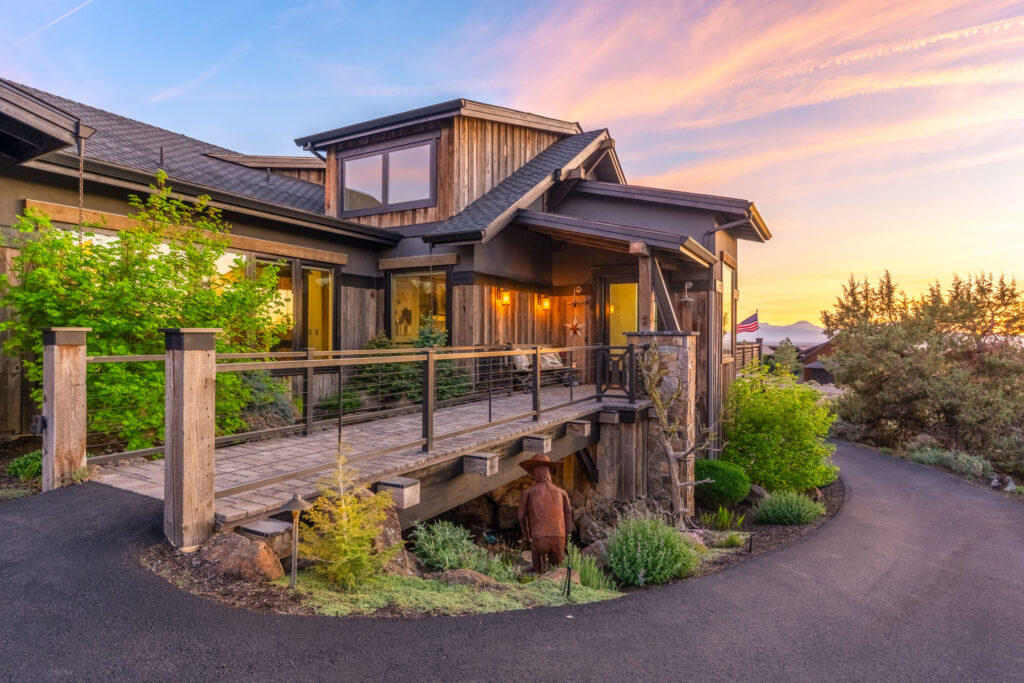 Dusk exterior of a rustic timber home with deck over landscaped high desert terrain
