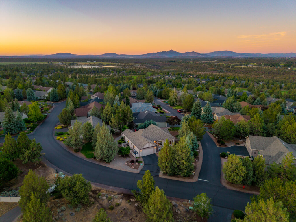 Aerial drone photo of a Bend, Oregon neighborhood at sunset with Cascade foothills on the horizon