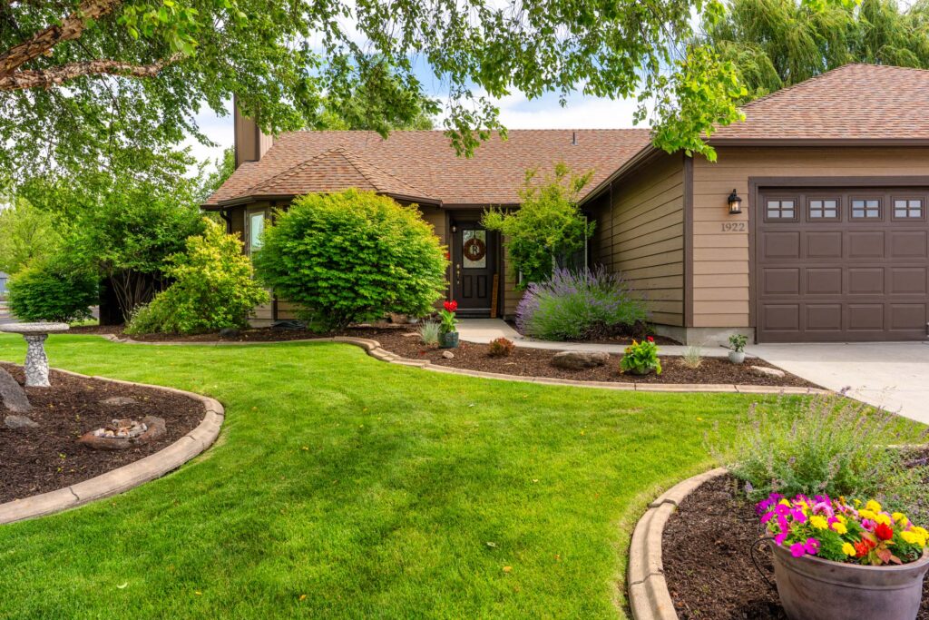 Front exterior real estate photo of a Bend, Oregon home with lush landscaping and summer flowers